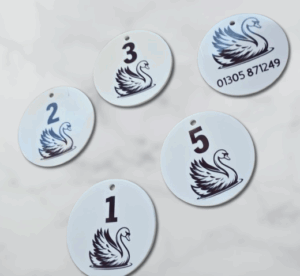White acrylic key tags numbered 1 to 5 with black swan logo, arranged on a white marble background.